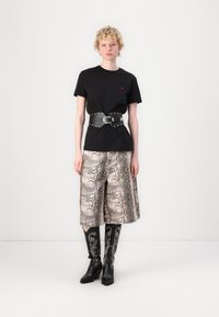 Svart T-skjorte med en liten rød logo, kombinert med beige culotter med slangeskinsmønster og svarte støvler med hvite dekorative sting.