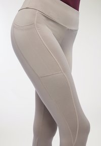 Beżowe legginsy sportowe z wysokim stanem, gładkim materiałem, szwem płaskim i detalami szwów wzdłuż ud, które zapewniają dopasowany wygląd.