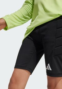 Svarta atletiska shorts i stretchigt tyg, med en texturerad panel och en vit logotyp. Kombineras med en ljusgrön långärmad skjorta.
