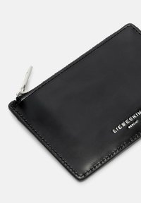 Czarny skórzany etui na karty o gładkiej fakturze, zaokrąglonych krawędziach i srebrnym zamku błyskawicznym. Z przodu wytłoczona nazwa marki w białym kolorze.