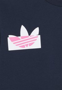 Tessuto di cotone navy con una grafica bianca bordata di rosa e strisce, che raffigura un logo con tre motivi a foglia.