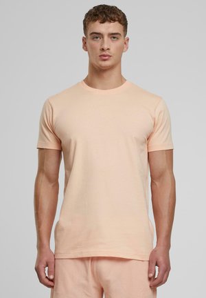 T-shirt en coton couleur pêche avec des manches courtes, col rond et coupe droite. Texture lisse, design minimal, sans motifs ni accents visibles.