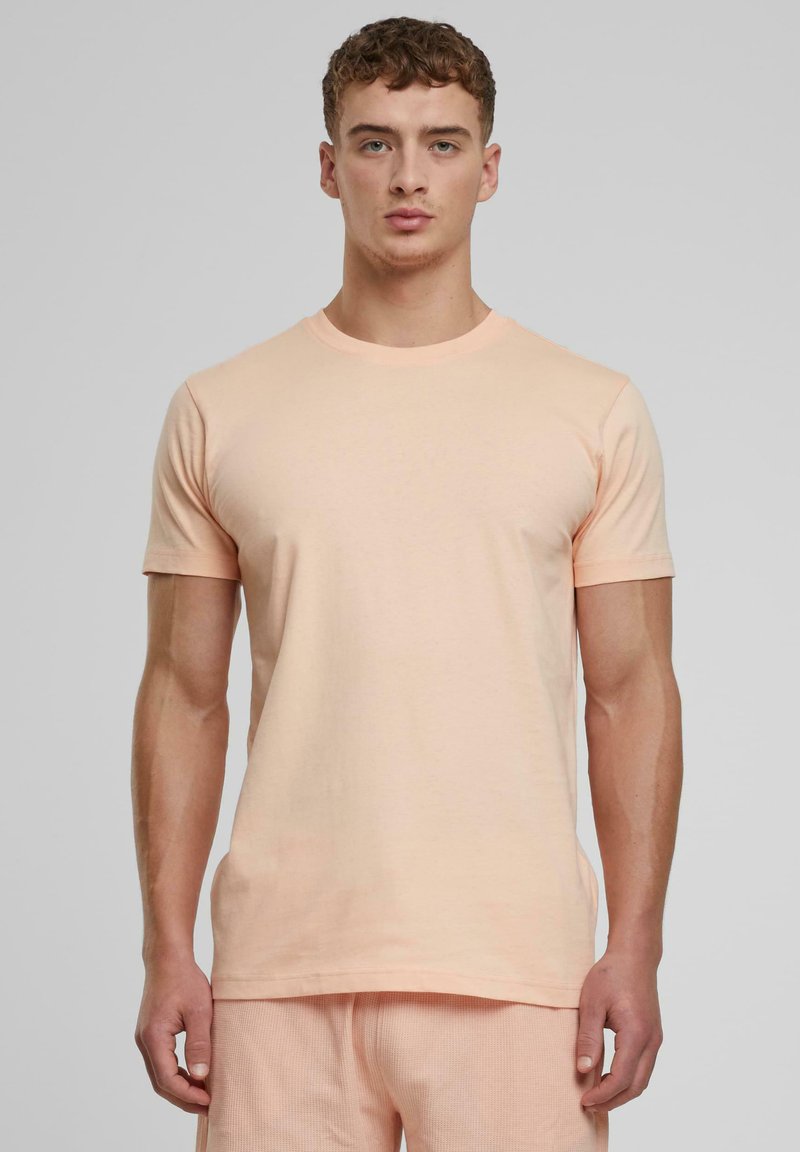 T-shirt en coton couleur pêche avec des manches courtes, col rond et coupe droite. Texture lisse, design minimal, sans motifs ni accents visibles.
