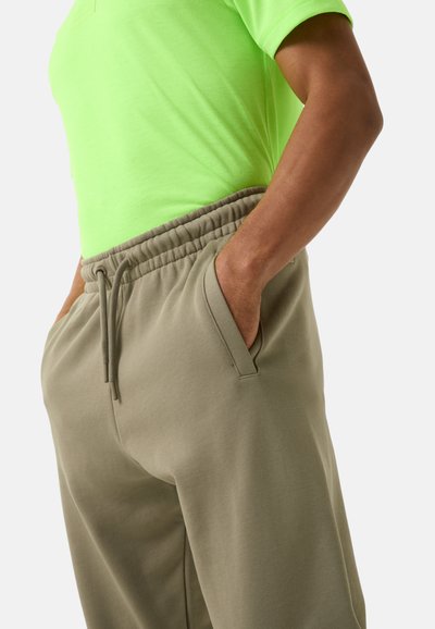 Neon groene T-shirt met korte mouwen, gecombineerd met beige joggingbroek met elastische tailleband en zijzakken, met een gladde stoftextuur.