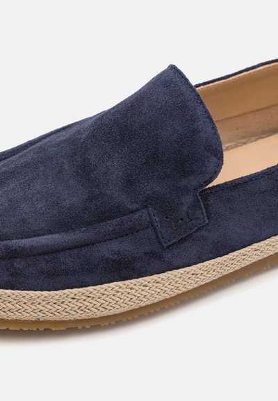 Chaussure slip-on en suede marine, dotée d'une semelle en jute tissé. Bout arrondi, texture lisse et accents de couture minimalistes sur le dessus.