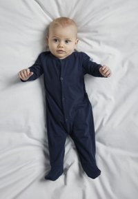 Mörkblå babyoverall i mjukt tyg, med långa ärmar, tryckknapp framtill och fothällor, liggande på en vit filt.