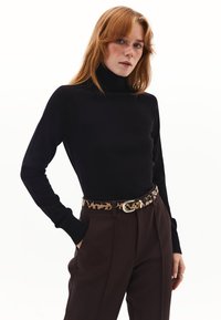Schwarzer Rollkragenpullover mit taillierter Silhouette, kombiniert mit hochgeschnittenen braunen Hosen und einem Gurt mit Leopardenmuster und silberner Schnalle.