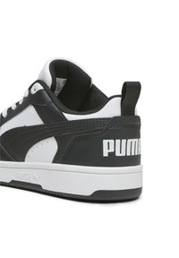 Svart och vit lädersneaker med rund tå, vita snören och texturerade detaljer; har en framträdande vit "PUMA"-logotyp på hälen.