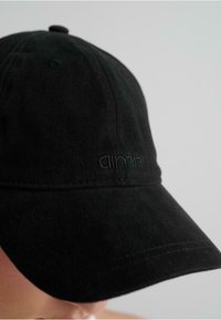 Gorra de algodón negra con visera curvada, detalles cosidos y un logo en relieve en el panel frontal. Superficie texturizada con un diseño minimalista.