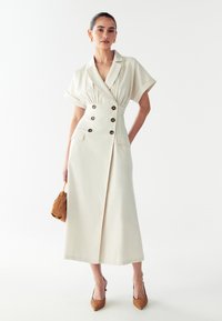 Kreemikaalune midi kleit, millel on kraelapid, lühikesed varrukad, kahekordne nööpraud ja taskud. Kombineeritud beežide kontsade ja pruuni kotiga.