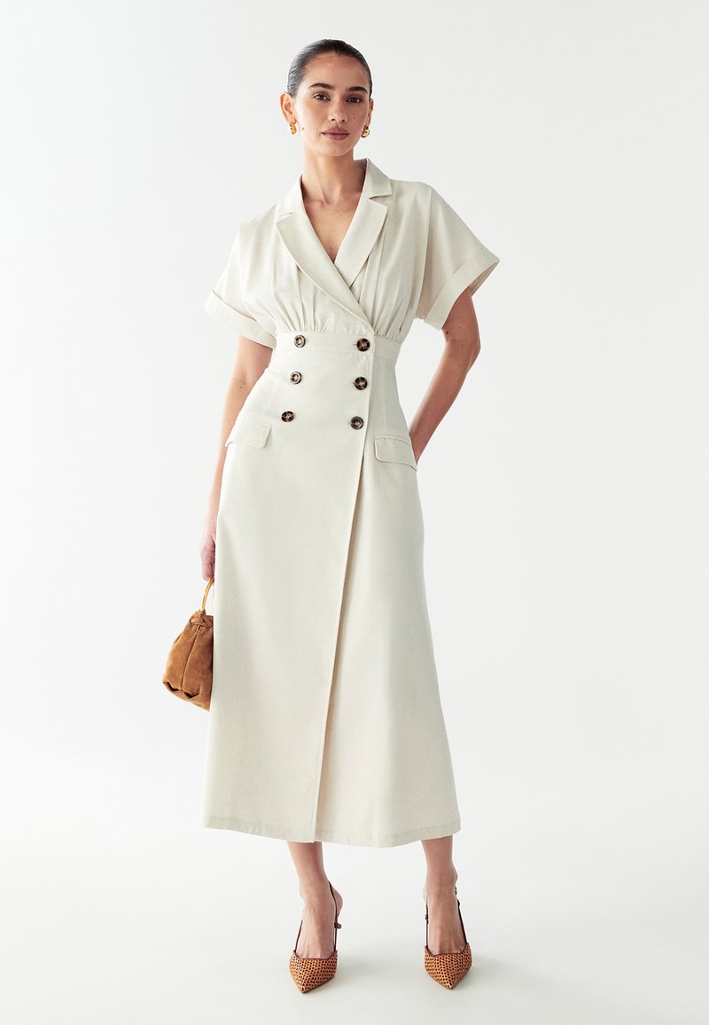 Kreemikaalune midi kleit, millel on kraelapid, lühikesed varrukad, kahekordne nööpraud ja taskud. Kombineeritud beežide kontsade ja pruuni kotiga.