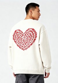 Roomkleurige sweatshirt met een groot rood hartontwerp dat is opgebouwd uit kleine, abstracte letters en vormen. Geribbelde manchetten en zoom.