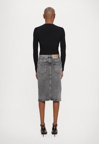 Top de manga longa ribalta preta combinado com uma saia midi de ganga cinza com bainha desnivelada, dois bolsos traseiros e um distintivo de couro com marca na cintura.