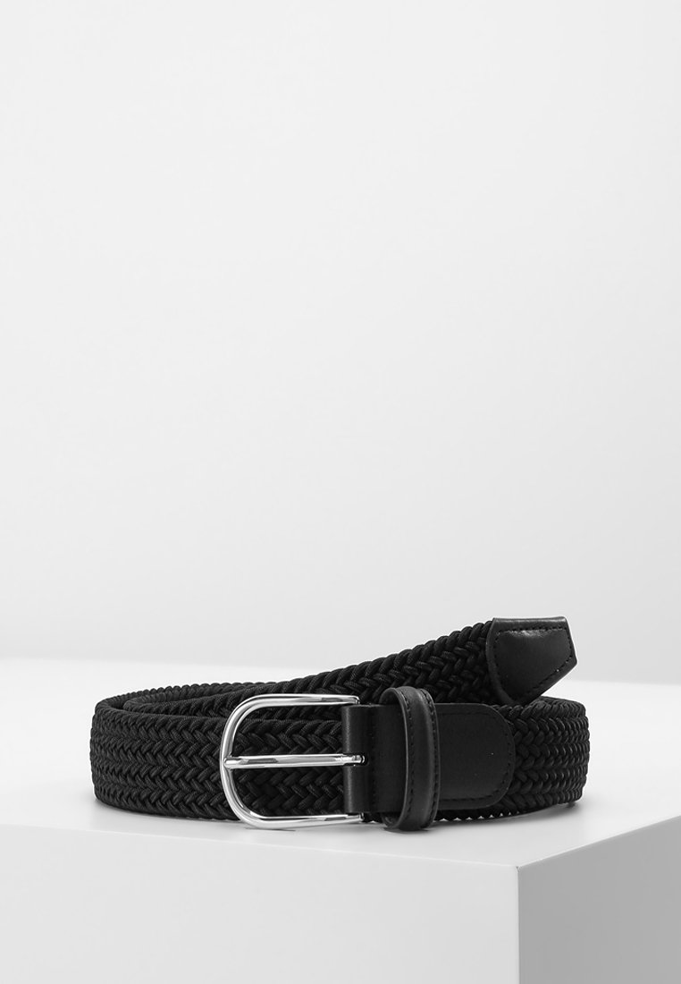 Ceinture tissée noire avec boucle en métal argenté, extrémité en cuir et passant, enroulée sur une surface blanche d'angle.