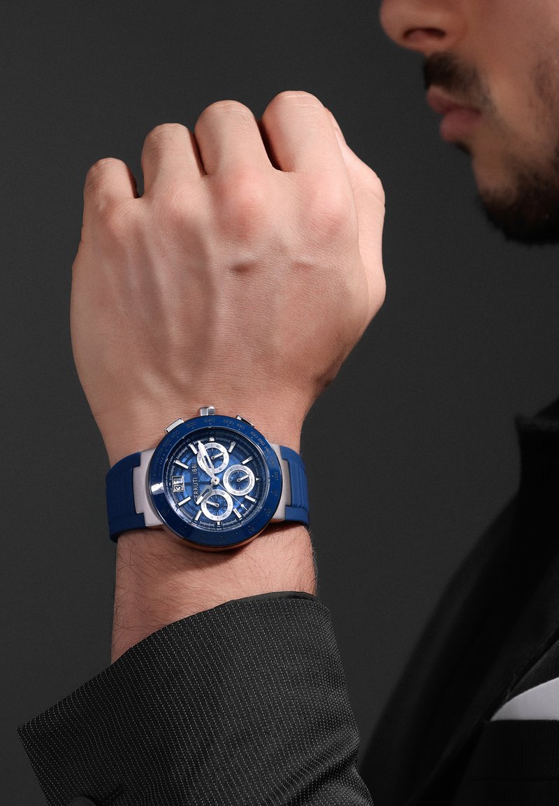 Orologio analogico blu con quadrante rotondo, cinturino in gomma e dettagli in argento. Presenta tre sottodial e un display per la data, il tutto su uno sfondo grigio.