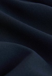 Tmavomodrá látka s hladkou, matnou textúrou, ktorá zobrazuje jemné vlny a záhyby, zdôrazňujúc jej mäkké a pružné vlastnosti.