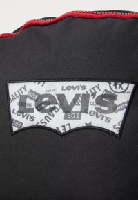 Fekete szövet piros cipzárral, amelyen egy fehér folt található, a Levi's logójának formájában. A folton a "Levi's 501" szöveg látható különböző mintákkal.
