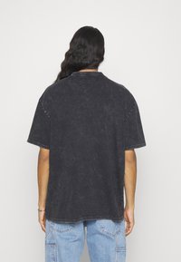 Sort oversized T-shirt med en falmet struktur, kortærmede og rund hals. Har synlige stikninger langs ærmerne og kanten.