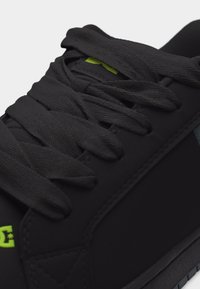 Κοντινό πλάνο μαύρου αθλητικού παπουτσιού με παχιά μαύρη κορδόνια και μικρό πράσινο λογότυπο κοντά στη μύτη και τη γλώσσα.