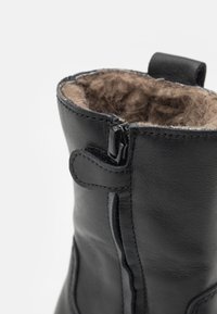 Svart läderankelstövel med blixtlås och en ögla för enkel påtagning. Inuti fodrad med mjukt, beige, strukturerat material för komfort.