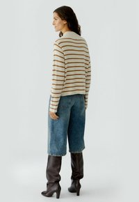 Gestreifter Pullover in Creme und Braun, verkürztes Design; kombiniert mit weiten blauen Jeansshorts. Das Modell trägt kniehohe braune Stiefel mit Absatz.