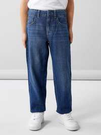 Vaqueros de denim azul con un corte relajado, que presentan un cierre de botón, dos bolsillos frontales y un diseño de pierna recta, combinados con zapatillas blancas.
