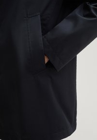 Marineblaue, leichte Jacke mit glatter Textur, seitlicher Tasche und klassischem Schnitt mit geradem Saum.