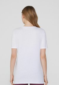 Camiseta de algodón blanca con mangas cortas y un escote redondo, que presenta una textura suave y un diseño de corte recto.