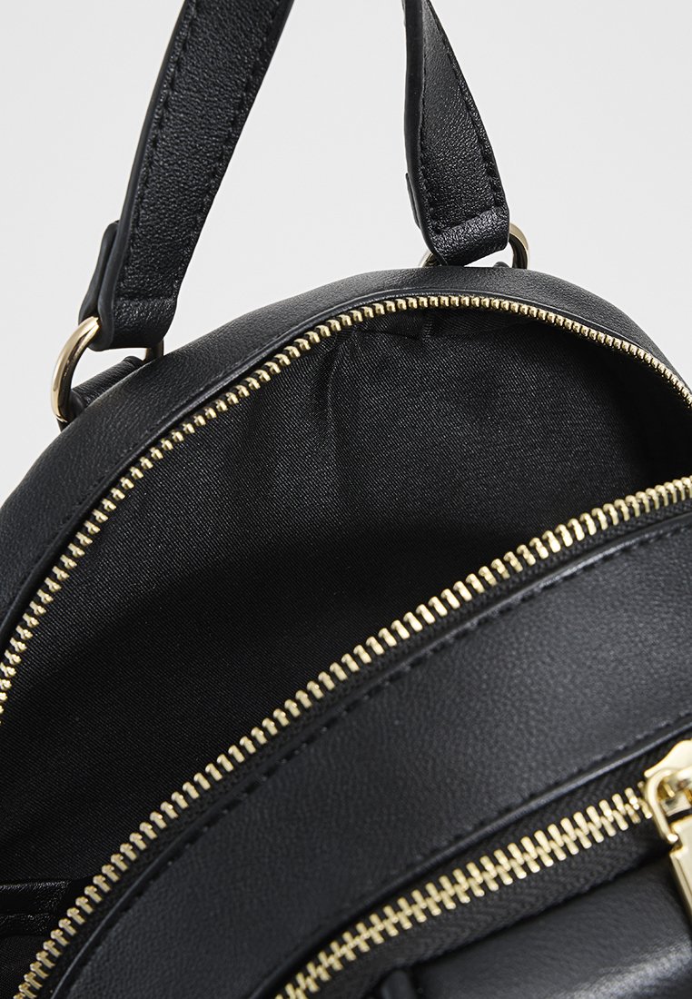 Schwarzer Kunstleder-Rucksack mit goldenen Details, der eine kreisförmige Form und zwei Reißverschlüsse hat. Das Innere ist mit einem glatten schwarzen Stoff ausgekleidet.