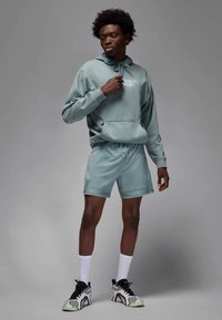 Vaaleanvihreä huppari kengurutaskulla ja kiristysnyörillä, yhdistetty samansävyisiin shortseihin. Mustavalkoiset tennarit, joissa on kuvioitu pohja.