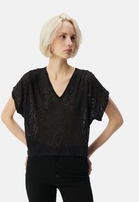 Top negro de manga corta con escote en V y textura de leopardo transparente. Se combina con pantalones negros de cintura alta con detalle de botones.