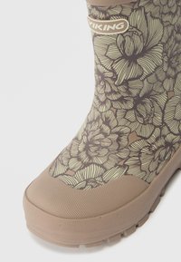 Bota de borracha castanha com padrão floral, acabamento texturizado e um detalhe bege na ponta. O logótipo perto do topo destaca a identificação da marca.