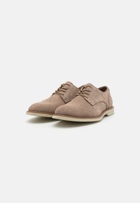 Zapatos de ante marrón con cordones, puntera redondeada, textura suave, suelas de goma beige y sutiles acentos de costura.