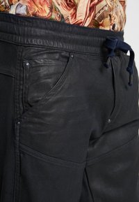 Pantalones negros con una superficie texturizada, que cuentan con cintura con cordón, bolsillos laterales y detalles metálicos. Diseño casual, adecuado para el uso diario.