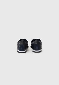 Sötétkék bőrsneaker texturált felsőrésszel és sima sarokkal. Fehér gumitalp és minimális márkajelzés a hátsó részen.