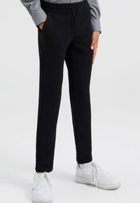 Svarta stickade byxor med strukturerad tyg, med dragsko i midjan och sidofickor, parat med vita sneakers.