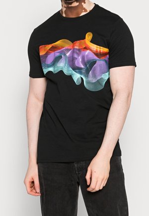 Man draagt een zwart T-shirt met een kleurrijk abstract golvend patroon in oranje, paars en teal over de borst, gecombineerd met een zwarte broek.