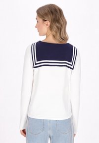 Maglia a maniche lunghe con il corpo bianco e colletto da marinaio blu navy con strisce bianche. Texture morbida; design nautico classico.