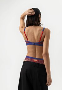 Kanten bralette in diep rood en donkerblauw met verstelbare bandjes en een haaksluiting, gecombineerd met een bijpassende kanten thong met contrasterende accenten.