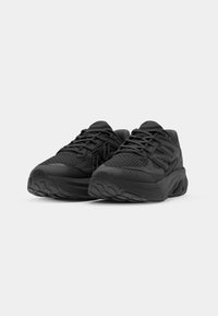 Black athletic shoes with a mesh upper, textured rubber sole, and reinforced toe. Features a lace-up design and subtle branding accents.