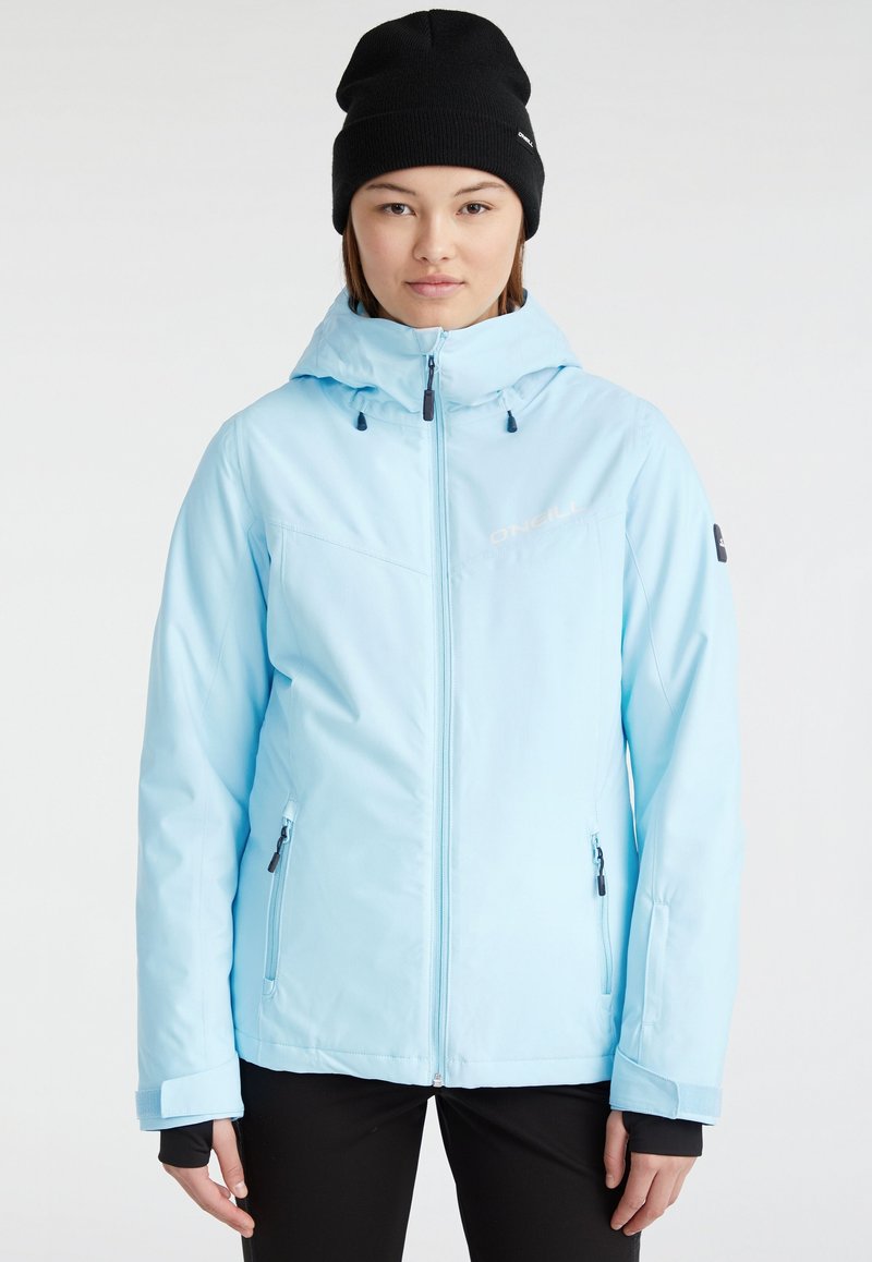 Giacca impermeabile azzurro chiaro con cappuccio, chiusura con zip, due tasche laterali e polsini elasticizzati. Berretto nero di maglia indossato sulla testa.