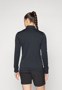 Zwart langwerpig shirt met een kraag, met een zachte textuur en zijzakken, gecombineerd met zwarte shorts.