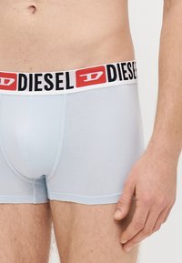 Gaiši zili bokseršorti no elastīga auduma ar melnu un sarkanu, zīmolu rotātu jostu ar atkārtotu tekstu. Gluda tekstūra un pieguļošs dizains.