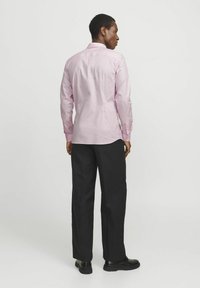 Helles rosa Langarmhemd mit Button-Down-Kragen, schlanker Schnitt und Rückenpasse, kombiniert mit schwarzen Hose und schwarzen Schuhen.