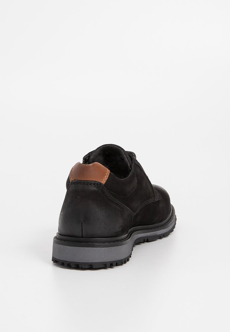 Scarpa in pelle nera con un accento marrone sul tallone, suola in gomma con trazione e design a punta arrotondata. Texture opaca con cuciture minime.