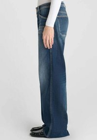 Jeans de mezclilla azul claro con un diseño de pierna recta y un ligero desgaste. Presentan un estilo tradicional de cinco bolsillos y un cierre de cremallera.