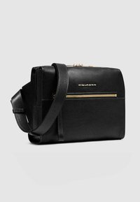 Borsa a tracolla in pelle nera con texture liscia, chiusura con cerniera e tasca frontale con zip, caratterizzata da un logo dorato e tracolla regolabile.