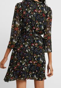 Vestido floral de tejido negro semitransparente con un estampado vibrante de flores rojas, azules y blancas. Tiene un cinturón y mangas de tres cuartos.