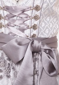 Lavendelfarbenes Korsettkleid mit satinierter Ribbonschnürung vorne, kunstvollen silbernen Verschlüssen, floralem Stickereien und einer großen satinartigen Schleife in der Taille.