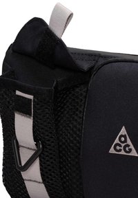 Sac en tissu noir avec une poche latérale en maille, une boucle grise, un clip noir en forme de triangle et un logo "acg" sur le panneau avant.